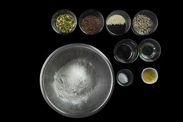 Ingredients for the preparation of healthy bread: whole-grain rye flour, sunflower oil, honey, sunflower seeds, sesame seeds, pumpkin seeds, flax seeds on a black background, flat lay, top view