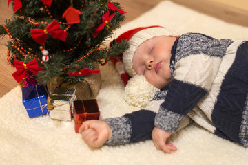 Little baby in Santa's hat sleeping under the Christmas tree
