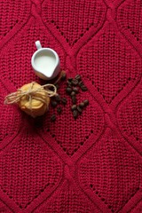 Coffee beans with milk, pile of delicious chip cookies tied with twine on a red knitted background with a pattern. Good morning concept. Enjoy slow life