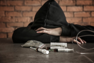 Female junkie with drugs at grey table. Concept of addiction
