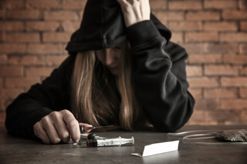 Female junkie with drugs at grey table. Concept of addiction
