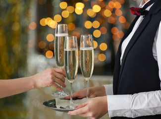 Woman taking glass of champagne from tray of waitress at party