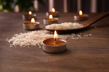 Burning candles and spoon with sea salt on wooden table