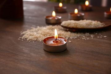 Burning candles and spoon with sea salt on wooden table