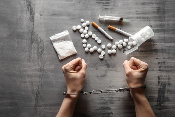 Female junkie in handcuffs with drugs and syringe on grey background. Concept of addiction