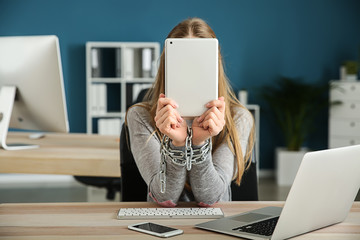 Woman with chained hands and modern devices at wooden table. Concept of addiction