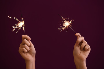 Woman holding Christmas sparklers on color background