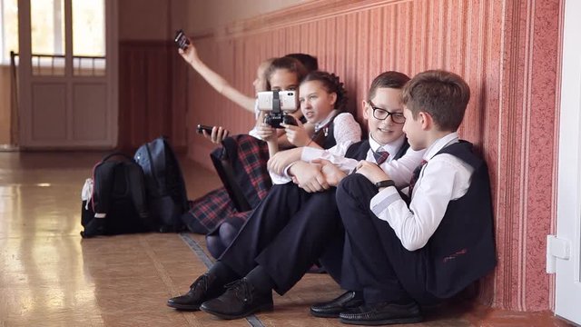 Selective focus of miserable schoolboy in uniform sitting alone on floor in school hallway with head on knees crying and feeling lonely, chatting and laughing classmates in background then a classmate