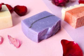 Handmade soap bars and flower petals on color background