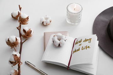 Burning candle, cotton flowers and open notebook with text NEW DAY NEW LIFE on white background