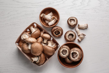 Bowls and basket with fresh raw mushrooms on light table