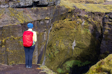 A young woman with a red backpack admires the view of the waterfall. Huge streams of water fall from the rocks. Iceland Europe