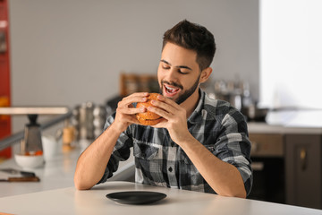 Young man eating tasty burger at home