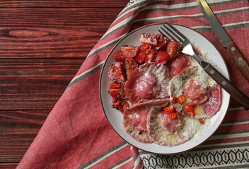 Plate with tasty ravioli on wooden table, top view