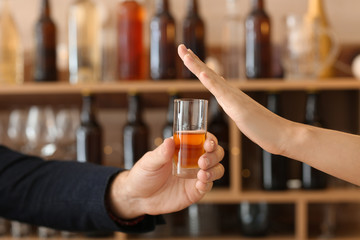 Man with glass of whiskey and woman refusing to drink in bar