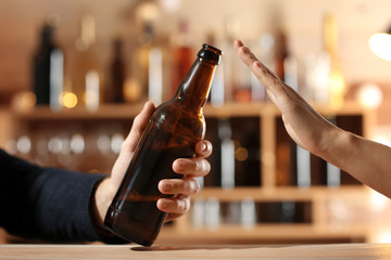 Man with bottle of beer and woman refusing to drink alcohol in bar