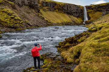 A young woman with a red backpack admires the view of the waterfall. Huge streams of water fall from the rocks. Iceland Europe