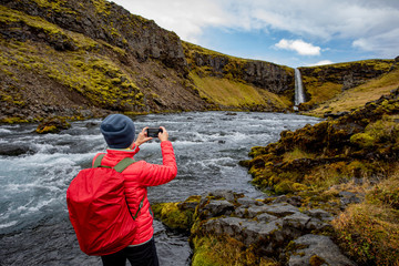 A young woman with a red backpack admires the view of the waterfall. Huge streams of water fall from the rocks. Iceland Europe