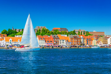 Beautiful panorama of a European port city. A yacht is sailing against the skyline of the city of Flensburg, Germany - obrazy, fototapety, plakaty