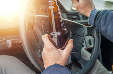 A drunken man driving a car with a bottle of alcohol in his hand.A man holds a driving wheel and a...