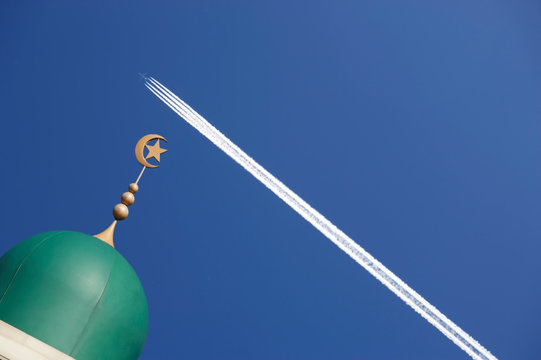 MOSQUE TOWER WITH JET AIRCRAFT VAPOUR TRAIL AGAINST BLUE SKY