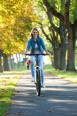 Fototapeta premium Young woman ride bike in autumn park. Enjoying while cycling in nature during autumn day.