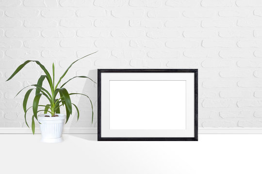 Photo frame mock up near white bricks wall and yucca plant in flower pot