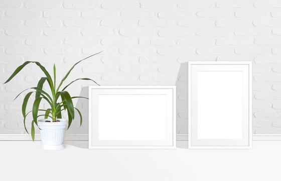 Two blank photo frames near white bricks wall and yucca plant in flower pot