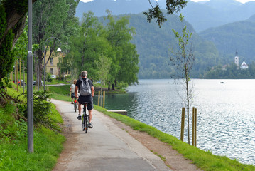 Beautiful Lake Bled in the Julian Alps and cycling tourist. Mountains, clear aquamarine water lake and dramatic blue sky.