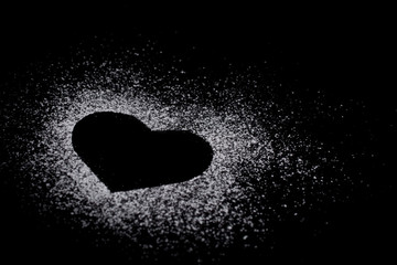 Heart shape made of icing sugar on total black background with copyspase. Concept of Valentine's day and sweet romantic love