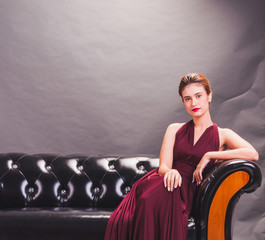 Fototapeta na wymiar Beautiful Asian woman wearing red dress sitting on a sofa