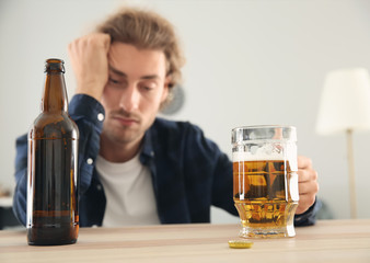 Depressed young man drinking beer at home. Alcoholism concept
