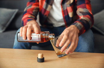 Man pouring alcohol from bottle into glass at table, closeup. Alcoholism concept