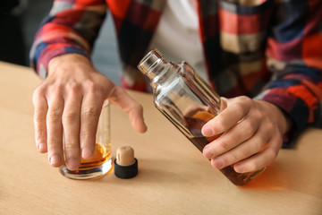 Man pouring alcohol from bottle into glass at table, closeup. Alcoholism concept