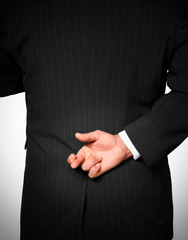 BUSINESS MAN WEARING DARK PINSTRIPE SUIT WITH FINGERS OF RIGHT HAND CROSSED BEHIND BACK