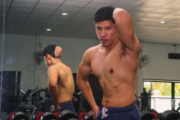 Fototapeta na wymiar Asian young man flexing his muscles in front of a glass in the gym.