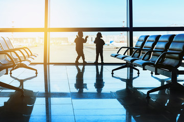 Silhouette of two children standing in the airport looking out the window