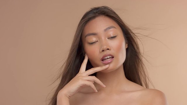 thai asian model frontal to camera with straight shiny hair blowing in air smiling and touches her face