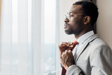 profile portrait of african american businessman adjusting red tie and looking at window © LIGHTFIELD STUDIOS