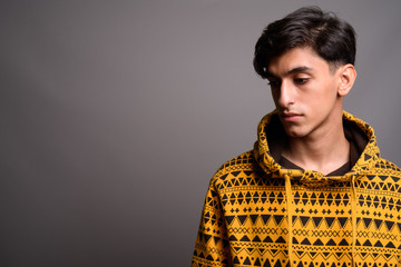 Sad young Persian teenage boy thinking against gray background