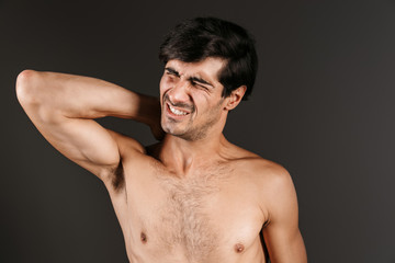 Obraz premium Handsome displeased young man with neck pain posing isolated over dark wall background.