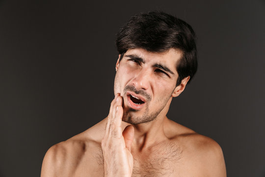 Displeased young man with toothache posing isolated over dark wall background.