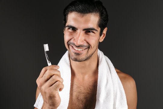 Handsome young man posing isolated over dark wall background brushing cleaning his teeth.