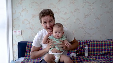 Father and baby saying hello. Daddy plays with his infant daughter facing the camera. Mixed-blood girl bonding with dad. Reversed gender role father caring for children.