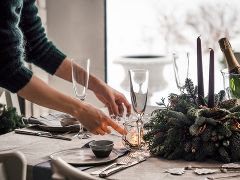 Female hands set the table for Christmas dinner in living room. Snowy winter in window on background. Beautiful served table with decorations, candles, fir branches. Holiday setting