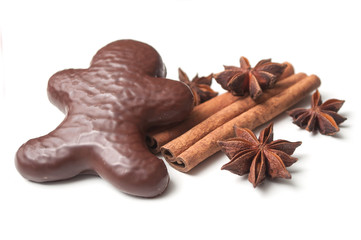closeup of christmas gingerbread chocolate coated biscuit in shaped man with anise flower and cinnamon stick on white background