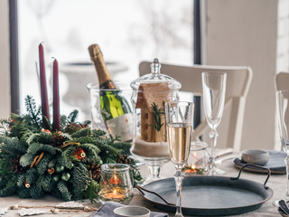 Close up view of table served for Christmas dinner in living room. Snowy winter in window on background. Beautiful served table with decorations, candles, fir branches. Holiday setting