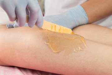 Removing unnecessary hair on the legs. Procedure sugaring in a beauty salon.Depilatory sugar paste