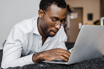 focused african american businessman in glasses working on laptop in hotel room