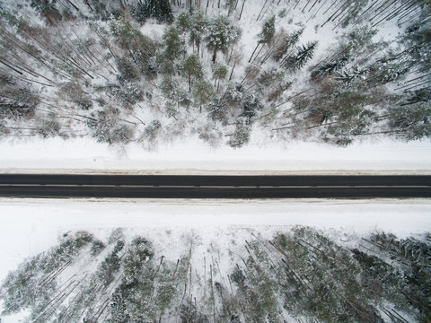 Winter forest and asphalt road. View from above. The photo was taken with a drone. Pine and spruce forest with a black road in the snow